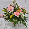 A mug arrangement with light pink carnations, spray roses and larkspur.