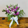 Purple tulips and white daisies in a glass vase with a white ribbon