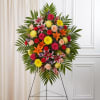 Standing spray arrangement with bright, mixed colors accented with soft, lush greenery