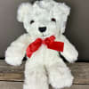 White plush teddy bear with a red bow sitting on a wooden surface