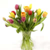 Two dozen assorted tulips stand alone in a clear glass vase.