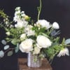 White floral arrangement in a silver vase on a wooden stand