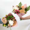 Two hand-held bouquets with peach, white, and pink flowers