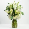 White floral arrangement in a glass vase with green accents