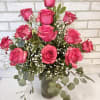 A dozen hot pink roses arranged in a vase with greenery and