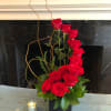 Red roses arranged in a tall black vase with curly branches