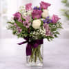 Bouquet of purple and white roses in a clear glass vase with a ribbon