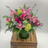 Pink calla lilies, orchids, and green hydrangeas in a clear glass vase on a wooden crate