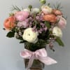 Pastel ranunculus arranged with fillers and greens in a small vase. (12
