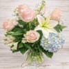 Pink roses and white lilies in a glass vase with blue hydrangea