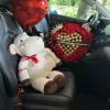 Red heart balloons, a plush cow, and a rose-and-chocolate gift arrangement in a car seat
