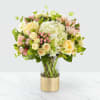 Bouquet of cream and pink flowers in a clear vase with a gold wrap