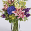 Bouquet of pink lilies, blue hydrangea, and purple flowers in a clear glass vase