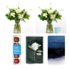 White floral arrangement in a glass vase with a chocolate box and sympathy cards nearby