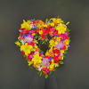 Heart-shaped standing wreath of bright yellow lilies, roses, carnations, and mums on a dark background