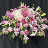 Pink and white floral spray with lilies, roses, and ribbon on a black backdrop