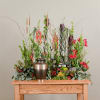 Tall floral arrangement with red and orange blooms in a bronze urn