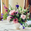 Mixed pink, purple, and white flowers arranged in a white vase