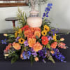 Colorful floral arrangement with roses, gerbera daisies, and blue delphinium around an urn