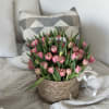 Pink tulips arranged in a woven basket with a white ribbon