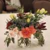 A warm, textural arrangement featuring roses, carnations, thistle, and seasonal greenery in