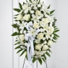 White floral standing spray with roses and lilies on a black easel