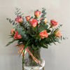 Pink-orange roses in a clear glass vase with eucalyptus and a ribbon