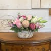 A pink centerpiece arrangement of white lilies, lavender and pink roses, pink
