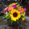 Bouquet of sunflowers, orange roses, and purple flowers in a glass vase
