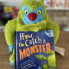 A green plush monster holding a children's book titled 