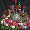 Floral arrangement with pink roses and mixed blooms around a decorative urn