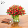 Red tulip bouquet in a clear glass vase on a wooden table
