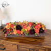 Long low floral arrangement with orange, red, and dark burgundy blooms in a wooden box