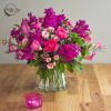 Pink and magenta floral arrangement in a clear glass vase with a pink candle holder nearby