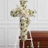 White floral cross on an easel beside a casket