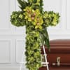 Green floral cross on an easel beside a casket