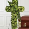 Green floral cross on a stand beside a casket