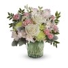 Pastel arrangement of cream roses, pink blooms, and green mums in a green glass vase