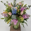 Tall pastel arrangement of pink roses, lilies, blue delphinium and stock in a clear glass vase