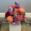Mixed bouquet of pink, peach, purple, and red flowers in a square vase