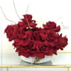 Low white bowl filled with clustered deep red roses and curly decorative branches