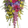 Standing floral spray with pink roses and purple flowers on a white easel