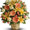 Mixed bouquet of yellow lilies, peach gerbera daisies, and white carnations in a woven basket