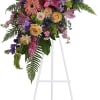 Standing floral spray with pink lilies, roses, and purple blooms on an easel