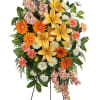 Standing floral spray with yellow lilies, orange daisies, and pink carnations