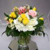 Bouquet of yellow and pink roses with white flowers in a clear glass vase