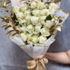 Bouquet of white roses and small daisy-like flowers wrapped in white paper with gold ribbon