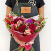 Handheld bouquet of red, pink, and purple roses with mixed filler flowers