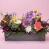 Mixed bouquet in a gray wooden box with purple, pink, white, and yellow flowers