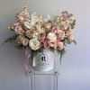 Large pastel pink and white flower arrangement in a white hat box on a clear stand